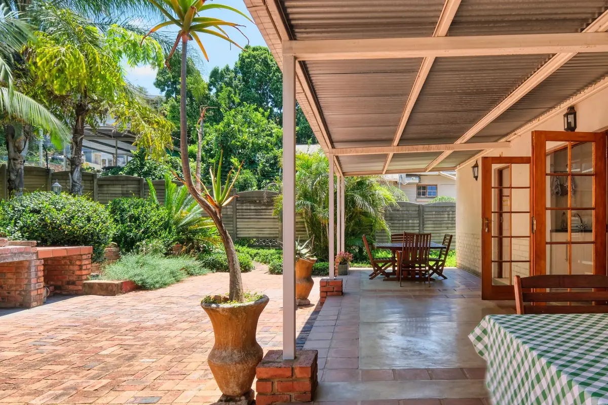 Metal-roofed patio cover over brick pavers beside a tropical garden